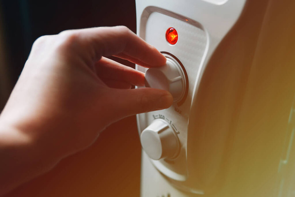 Hand adjusting the oil electric heater on at home. Cold winter, economic crisis concept. Home heating and heat conservation. Close-up. - Foto, Imagem