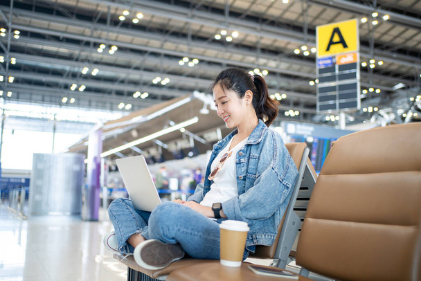 Attractive female tourist working with laptop in airport terminal. Freelancer student travels to business meeting. - Zdjęcie, obraz