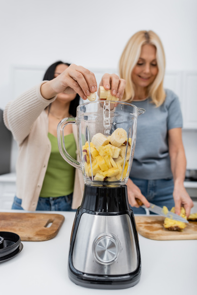 Blurred women cutting and pouring fruits in blender while making smoothie in kitchen  - Photo, Image