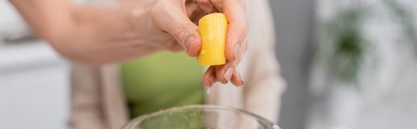 Ausgeschnittene Ansicht einer Frau, die Zitrone über dem Mixer in der Küche auspresst, Banner  - Foto, Bild