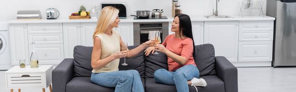 Amigos multiétnicos segurando champanhe enquanto conversam na cozinha, banner  - Foto, Imagem