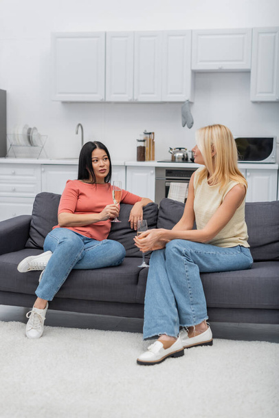 Interracial barátok pezsgővel beszél, miközben otthon ül a kanapén  - Fotó, kép