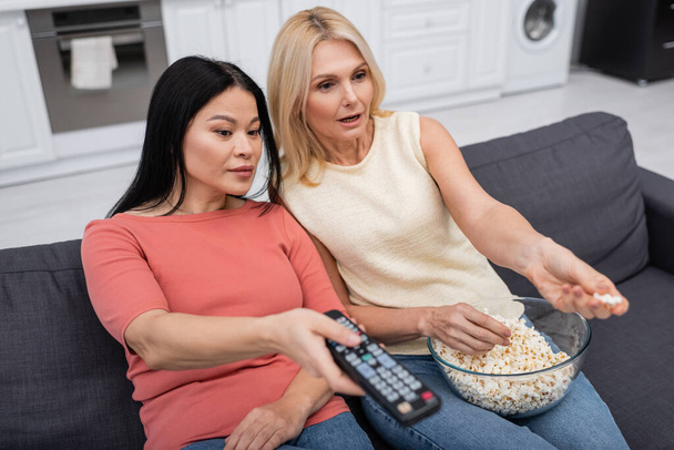 Amici multietnici con popcorn guardando film sul divano a casa  - Foto, immagini
