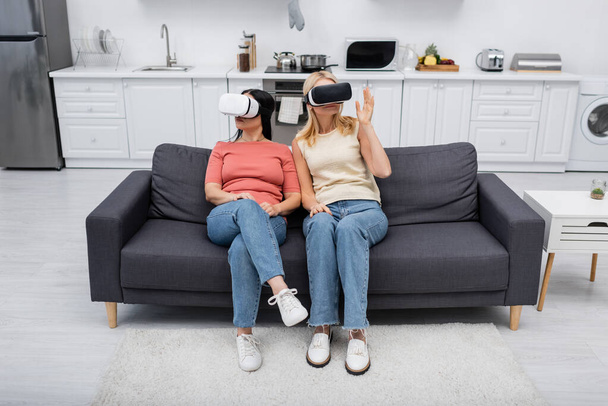 VR kulaklıklı kadınlar evlerinde oyun oynarken kanepede oturuyorlar.  - Fotoğraf, Görsel
