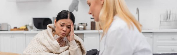 Nemocná asijská žena trpí bolestí hlavy v blízkosti rozmazané lékaře doma, prapor  - Fotografie, Obrázek