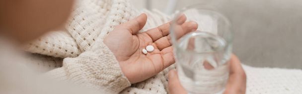 Vista cortada da mulher segurando pílulas e vidro borrado de água em casa, banner  - Foto, Imagem