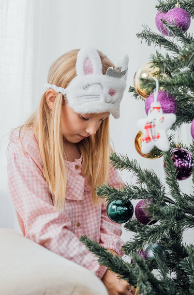 Egy kislány kényelmes pizsamában, karácsonyfát díszítve. - Igen. Kiváló minőségű fénykép - Fotó, kép