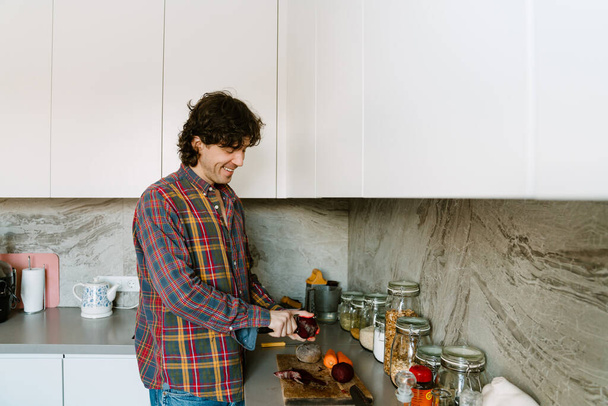 Valkoinen mies yllään paita leikkaamalla vihanneksia, kun ruoanlaitto lounas keittiössä kotona - Valokuva, kuva