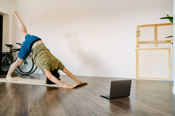 White man doing exercise during yoga practice with laptop at home - Photo, image