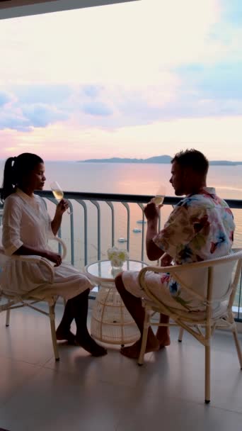 Een paar mannen en vrouwen dronken cocktails op het balkon van een hotel dat uitkeek over de oceaan tijdens zonsondergang in Pattaya Thailand..  - Video