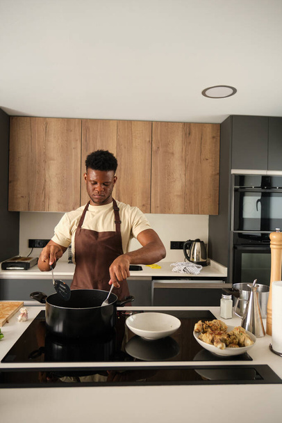 Young african man preparing fried chicken mince with vegetables recipe in a kitchen. - Photo, Image