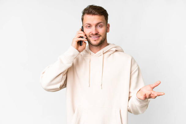 Young handsome caucasian man over isolated white background keeping a conversation with the mobile phone with someone - Foto, imagen