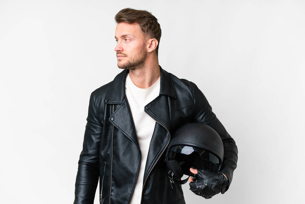 Jeune homme caucasien avec un casque de moto sur fond blanc isolé regardant vers le côté - Photo, image