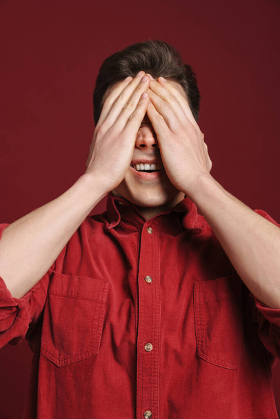 Young white man wearing shirt posing and covering his face isolated over red background - Foto, Imagem
