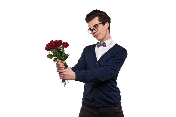 Young intelligent male with dark hair in classy clothes and eyeglasses smiling while standing against white background with bouquet of red roses in hands - Fotografie, Obrázek