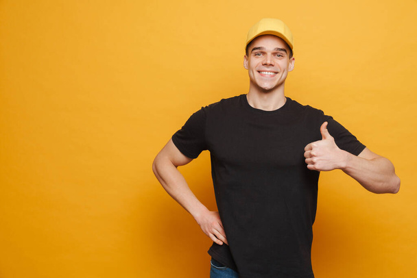 Young white man wearing cap smiling and showing thumb up isolated over yellow background - Foto, afbeelding