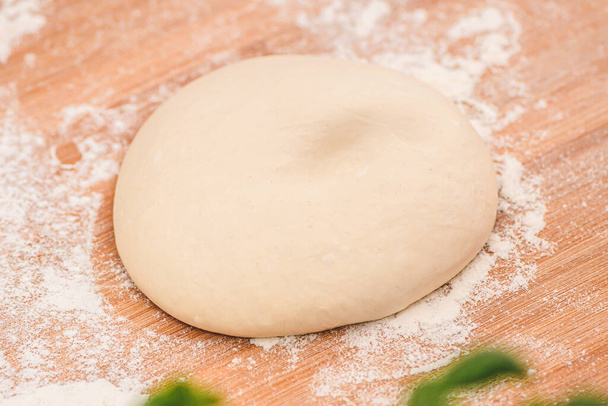 Dough for pizza on a wooden board with white flour and ingredients around ready for preparation, close up - Foto, Imagem