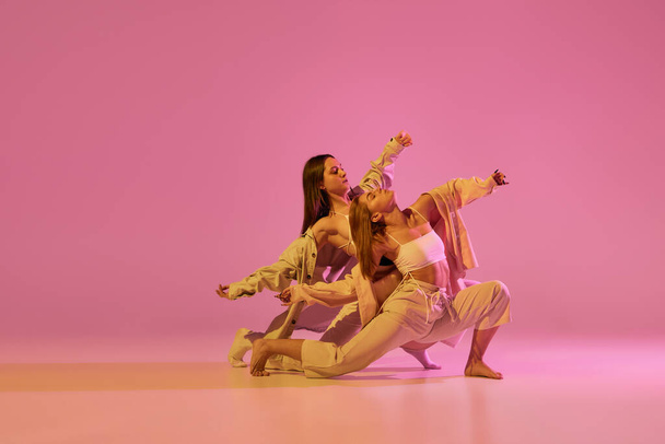 Сучасне танцювальне мистецтво. Молоді дівчата, пара танцюристів у спортивному одязі танцюють експериментальні танці, ізольовані на світло-рожевому фоні в неоні. Концепція музики, емоцій, танців. Копіювати простір для оголошення
 - Фото, зображення