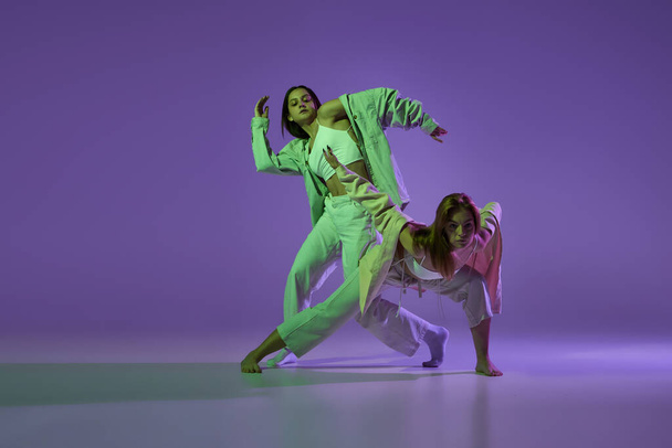 Experimental dance. Two young girl in motion, action isolated over purple background. Concept of new dance style, youth culture, music and fashion, ad, trends. Flexible and graceful dancers - Photo, Image