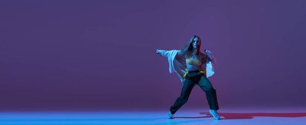 柔軟な若い女の子、現代のダンサーはネオンで暗い紫色の背景に隔離されたヒップホップや実験的なダンスを踊る。コンテンポラリーダンス。音楽、若者のライフスタイル、ファッション、スタイル。広告のコピースペース - 写真・画像