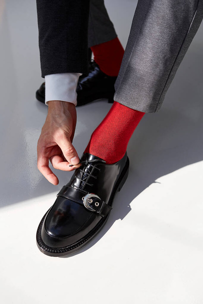 Egy férfi elegáns fekete cipőt visel piros zokniban, szürke alapon. - Fotó, kép