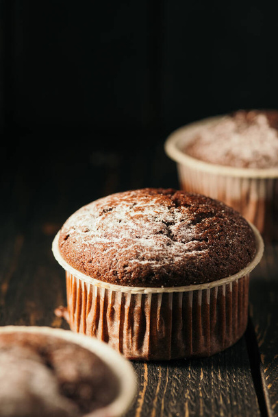 Chocolate muffins with powdered sugar on a black background. Still life close up. Dark moody. Food photo - Photo, Image