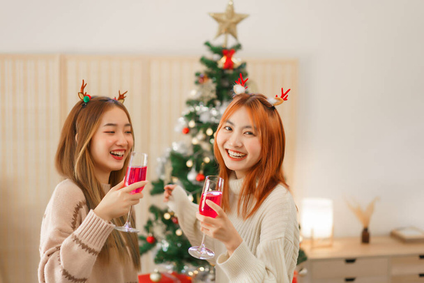 Χριστουγεννιάτικη ιδέα, Δύο γυναίκες πίνοντας σαμπάνια και χορεύοντας με την ευτυχία κοντά στο χριστουγεννιάτικο δέντρο. - Φωτογραφία, εικόνα