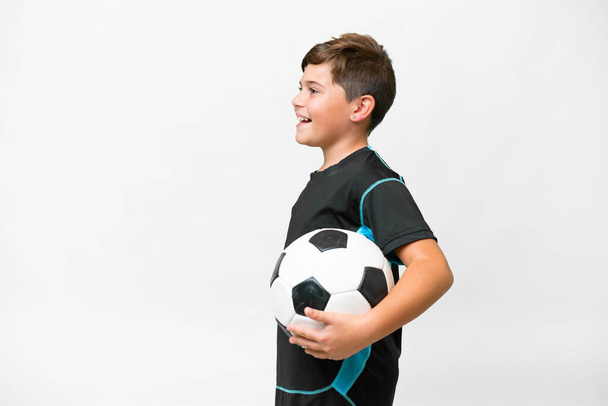 Pequeño jugador de fútbol caucásico niño sobre fondo blanco aislado riendo en posición lateral - Foto, imagen