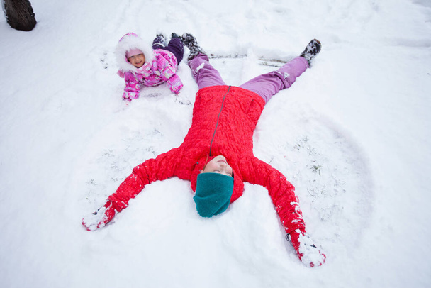 children lie on fresh snow and make a snow angel. Winter fun outside, family time in a snowy park - Photo, Image