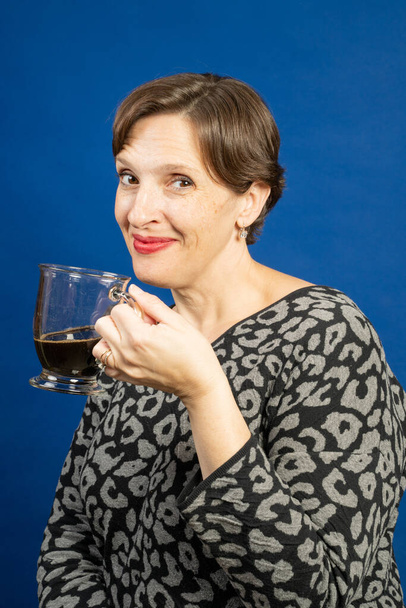 Mujer disfrutando de una taza de café negro. Foto de estudio de alta calidad fue tomada sobre un fondo azul. - Foto, Imagen