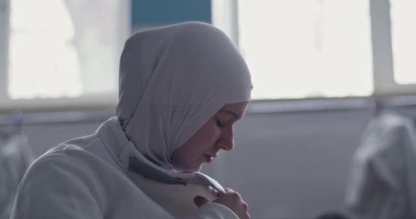 Basso angolo colpo palmare di recinzione femminile musulmana in hijab guardando altrove e fissaggio zoppo contro la finestra in spogliatoio illuminato dal sole di palestra - Filmati, video
