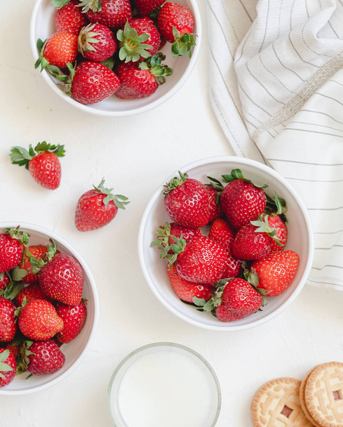 White bowls with fresh red strawberries, glass of milkand cookies. Healthy breakfast with berries. Top view. - Photo, Image