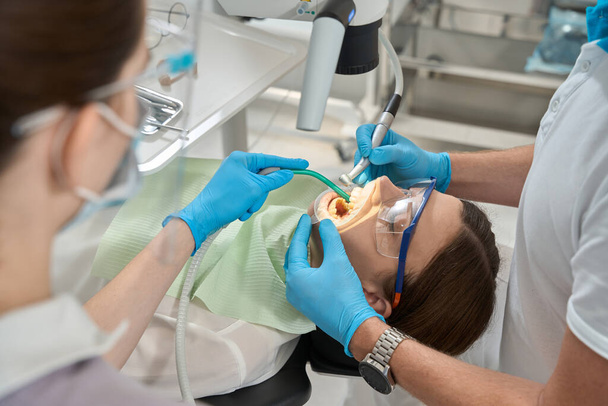 Stomatologist removing tartar between front teeth of young woman assisted by nurse - Photo, image