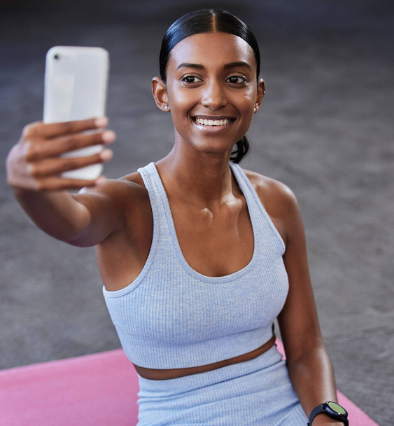 Fitness-selfie, urheilulattia ja nainen, jolla on sosiaalisen median viesti, profiilikuva päivitys tai wellness-verkkosivuston blogi mobiilisovelluksessa. Älypuhelin valokuvaus, Intialainen urheilija ja pilates tai sydän kuntosali koulutus. - Valokuva, kuva