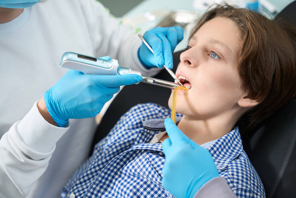 Hammaslääkärin tuolissa oleva lapsi saa ambulanssin hammassärkyyn, asiantuntija käyttää erikoistyökaluja. - Valokuva, kuva