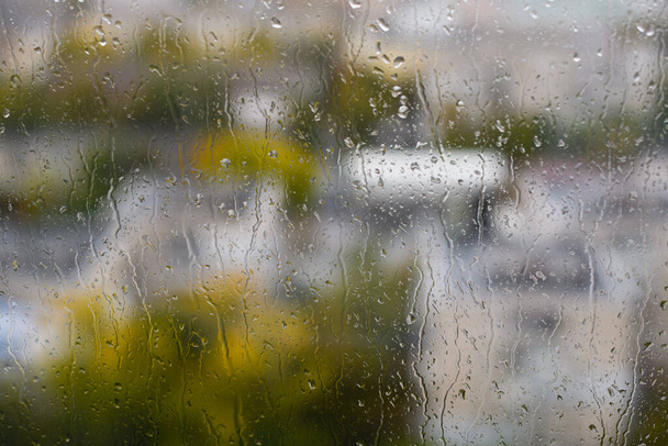Вид на размытый город через домашнее окно с капельками дождя. Сосредоточьтесь на капли дождя на стакане. - Фото, изображение