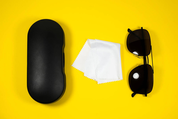 Чорна рамка чоловічих сонцезахисних окулярів з тканиною для чищення окулярів та футляром на жовтому фоні
. - Фото, зображення