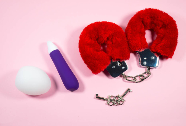 ピンクの背景にキーとバイブレータ付きの赤いセクシーなふわふわの手錠。エロティックセックスゲームとともに性的緊縛おもちゃ. - 写真・画像
