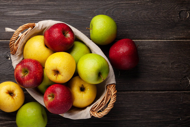 Coloridos frutos maduros de manzana en cesta sobre mesa de madera. Vista superior plano con espacio de copia - Foto, Imagen