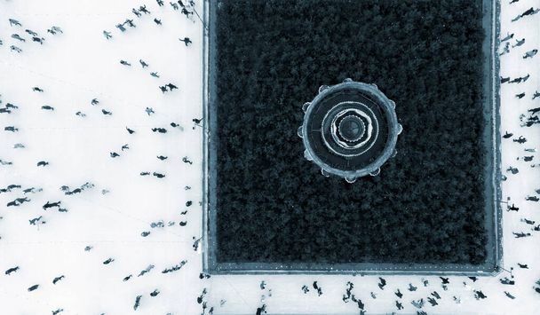 Aerial Drone View Flight Sok ember korcsolyázik szabadtéri jégpályán télen. Városi jégkorcsolyázás felülnézetből. City Park, Publik jégpálya. Tél kint. Korcsolyázás sport háttér Kék szín - Fotó, kép