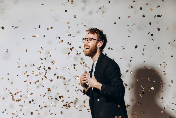 Tijd om te vieren. Portret van een gelukkige man dansend onder glinsterende confetti. - Foto, afbeelding