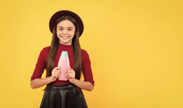 happy kid in hat hold hair conditioner bottle on yellow background, haircare. - Photo, Image