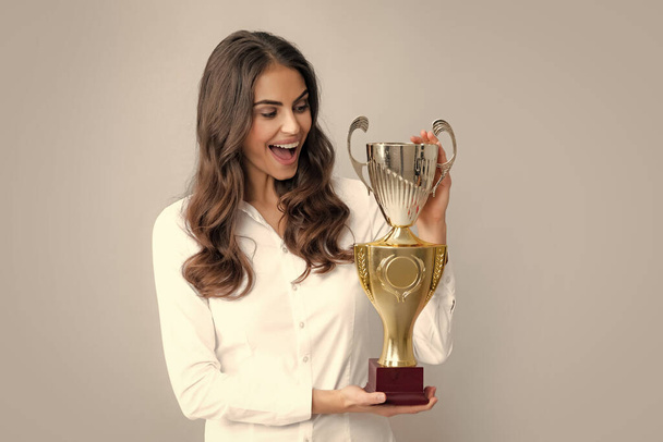 Winning businesswoman holding a trophy. Business woman with prize. Business woman with golden cup and fist up gesturing, isolated on gray. Concept of victory and success - Fotoğraf, Görsel
