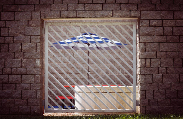 Kék-fehér csíkos esernyő rácsozott kerítés mögött. - Fotó, kép