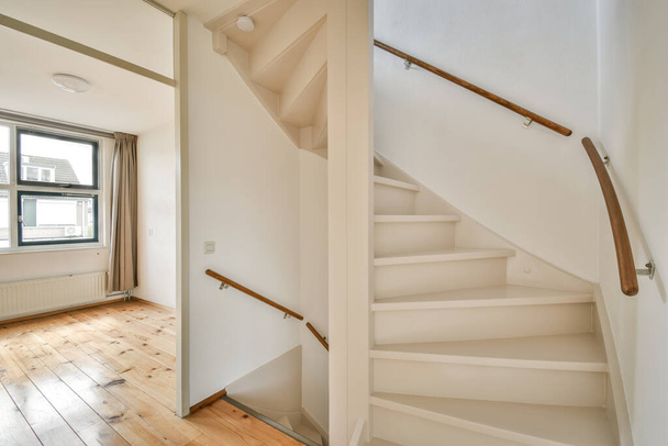 een lege kamer met houten vloer en wit geschilderde trap die leidt naar de tweede verdieping in een huis te koop - Foto, afbeelding