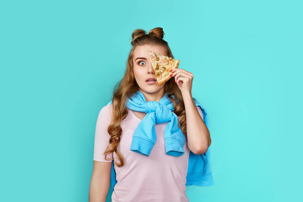 surprised woman covering her eyes with slice of fresh pizza on blue background. - Foto, Imagen