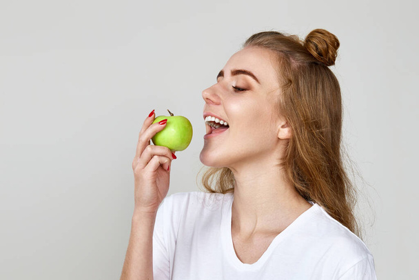 beautiful woman eating green apple on gray background. copy space - Photo, Image