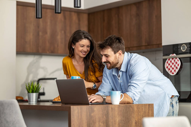Couple utilisant un ordinateur portable dans leur cuisine pour les affaires. Concept en ligne. - Photo, image