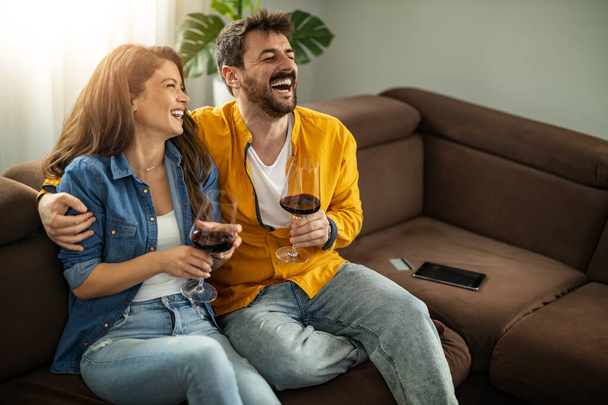 Young couple enjoying at home, drinking wine and celebrate anniversary. - Фото, изображение