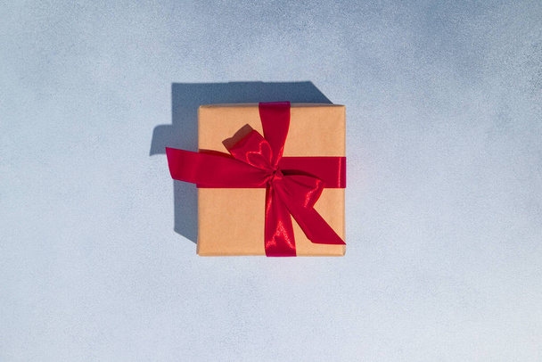 El işi ambalaj kağıdında kırmızı saten kurdeleli bir hediye kutusu. Tasarım için alanı kopyala. Yüksek kalite fotoğraf - Fotoğraf, Görsel